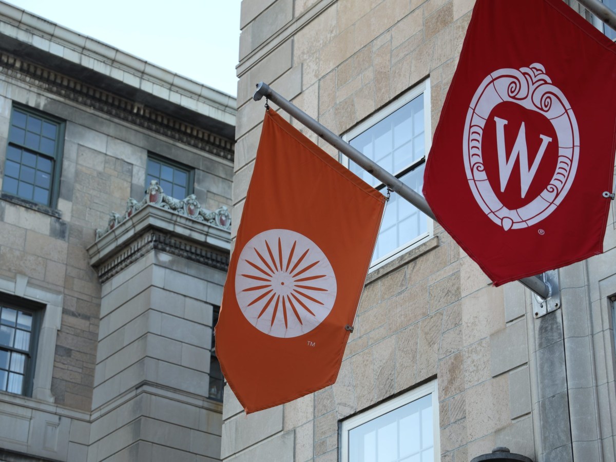 A banner with the Memorial Union logo and a banner with the University of Wisconsin-Madison logo waving in the wind.